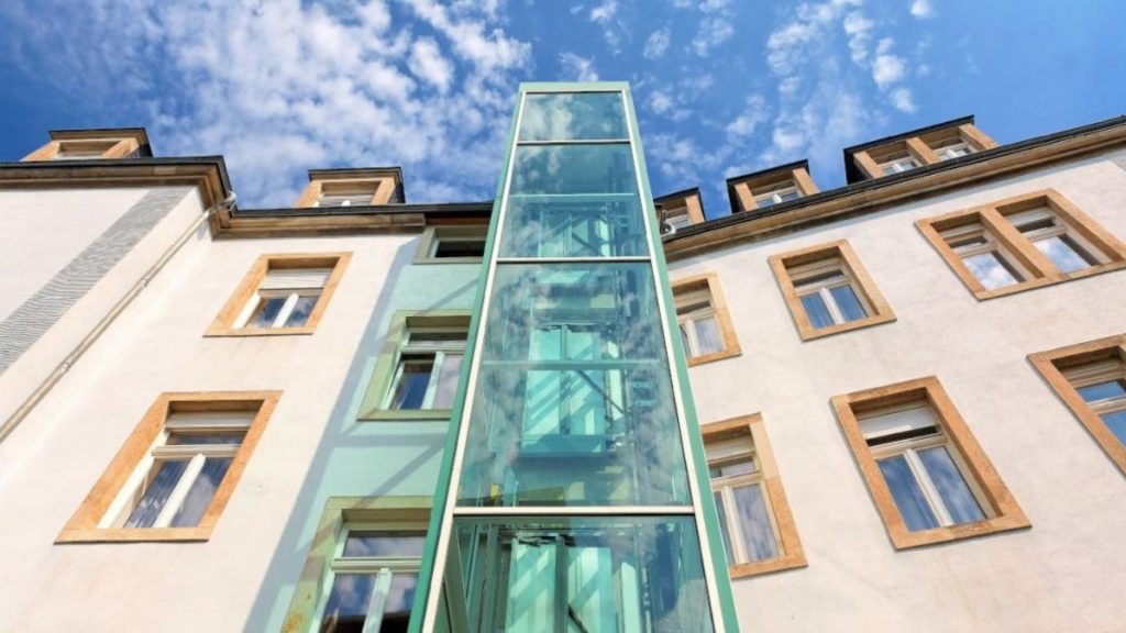 Aufzug nachträglich einbauen: Ein Glasaufzug ist an der Außenfassade eines Gebäudes angebracht.